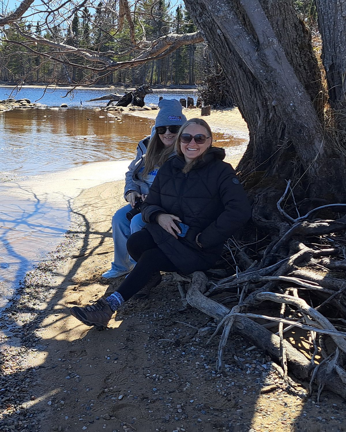 Two friends sitting together under a tree on a quiet lakeshore