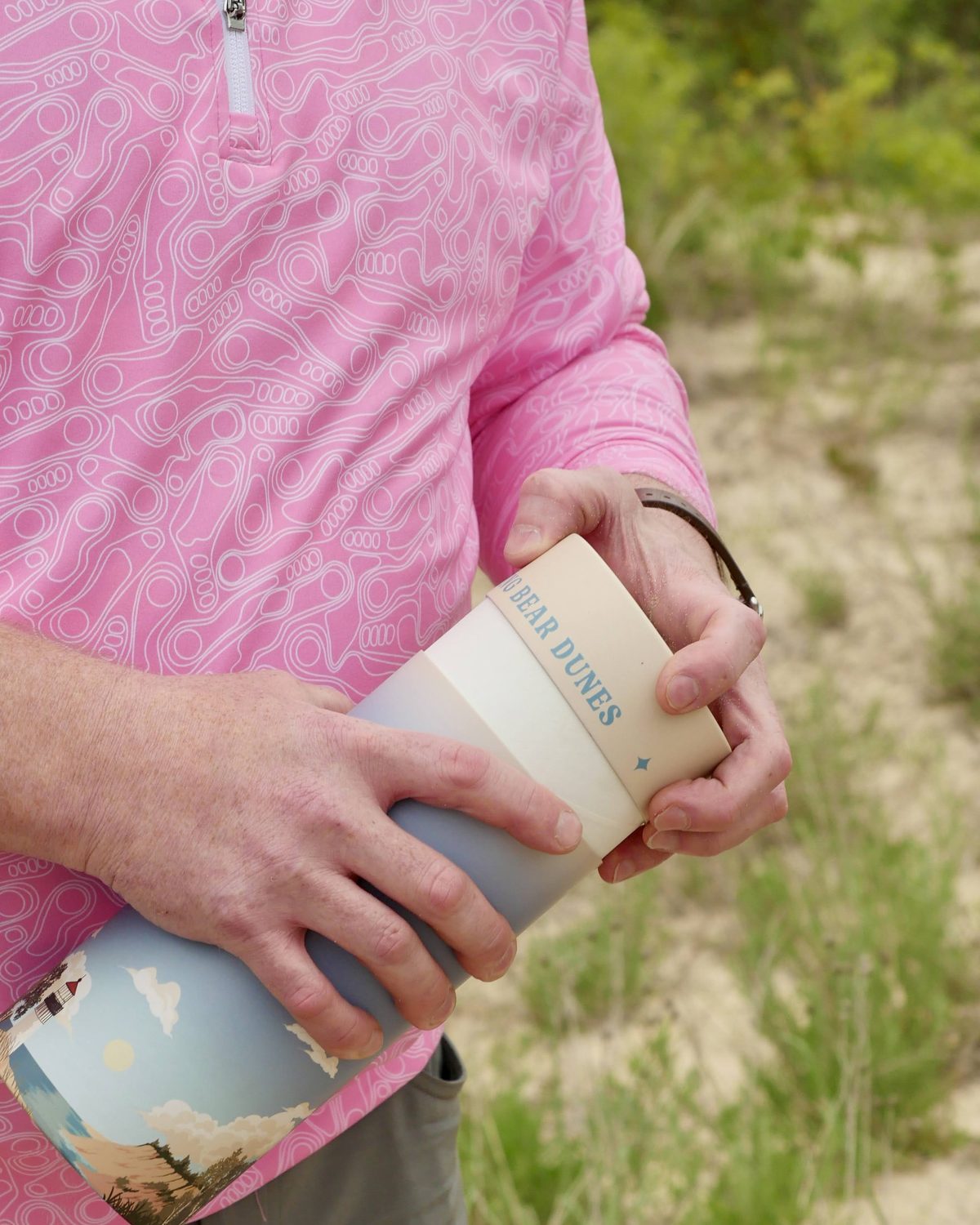 Hands holding a Sleeping Bear Dunes scattering urn on a sandy dune trail
