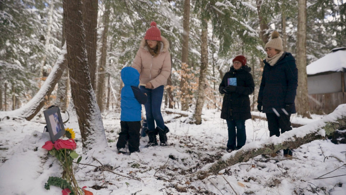 A family honoring their dog at a snowy forest memorial with flowers and a photo