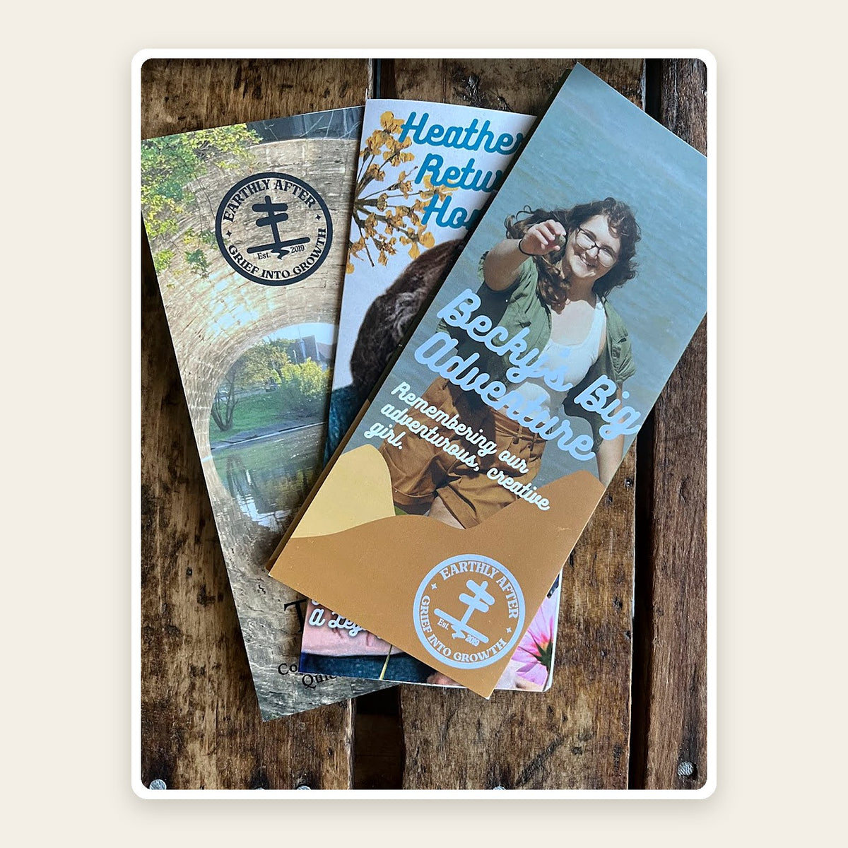 Three sample Final Adventure Maps, folded memorial guides with personalized photo covers, on a wood table