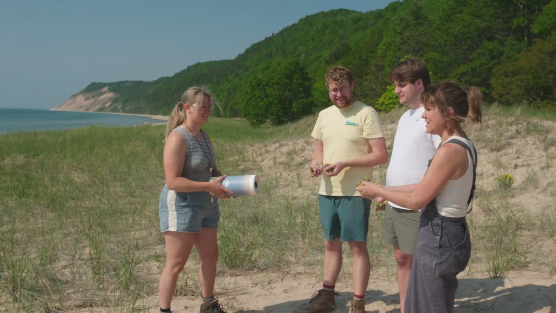 Friends laughing as they scatter ashes on a sunny dune above Lake Michigan
